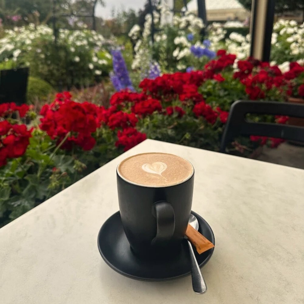 cappuccino coffee cup with a heart design on a saucer in front of garden flowers
